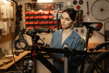Young female mechanic repairing bike in workshop or garage. Bike workshop interior.