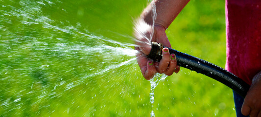 Hand and Hose Squirting Fresh Water on Grass - 780706128