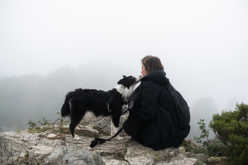 Young woman sitting on a rock playing with her border collie dog