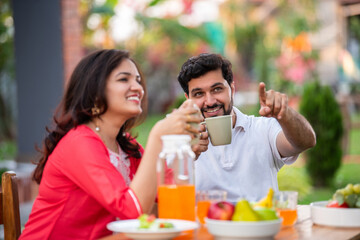 Attractive Indian young couple in love sitting at the cafe table outdoors, drinking coffee or tea,...