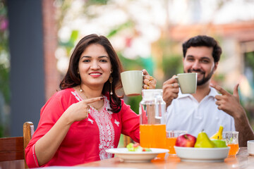 Attractive Indian young couple in love sitting at the cafe table outdoors, drinking coffee or tea, talking