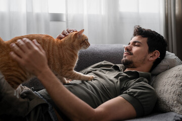 brown tabby cat interacts with a young man lying on a sofa