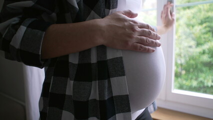 Close-up of mother caressing belly, expecting newborn child - 8 month pregnancy by residence window