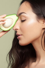 Young white woman with long dark hair showing cut avocado. Fruit, unsaturated fats, diet