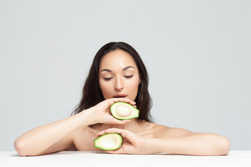 Woman sitting at white table on white background showing two halves of fresh avocado