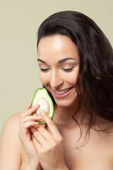 Young beautiful woman holding avocado half on pistachio background