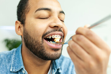 African American man with braces eating chocolate cake with a fork, man holding fork with food and...