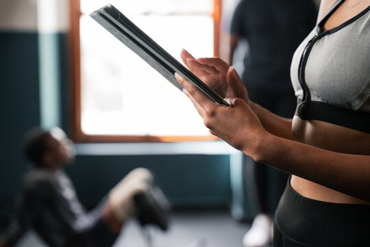 A woman in the gym is holding a tablet with her hands