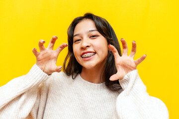 young asian girl with braces growls and pretends to be a tiger or cat on a yellow isolated...