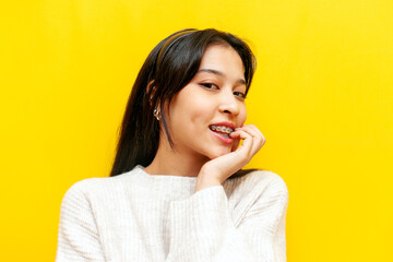 young pensive asian girl with braces flirts and thinks sexually over yellow isolated background,...