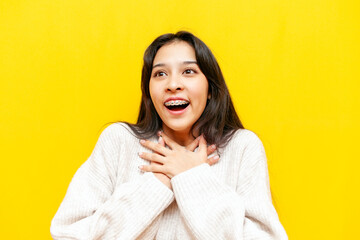 young shocked asian woman with braces wonders with open mouth on yellow isolated background, korean...