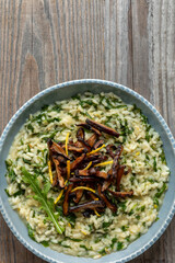 Lemon risotto with arugula and fried shiitake mushrooms in a blue bown on rustic wooden table. Copy space. 