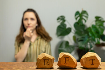 Letters EFT written on wooden blocks. Female tapping  chin (CH) meridian point in blurred background. Emotion-focused therapy treatment concept.