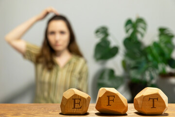 Letters EFT written on wooden blocks. Female tapping  top of head (TH) meridian point in blurred background. Emotion-focused therapy treatment concept.