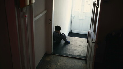 Little Boy in Crisis, Seated Alone in Shadowy Home Hallway, Hiding Face in Hands, Experiencing Deep...