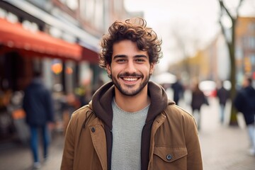 A man with curly hair is smiling and wearing a brown jacket