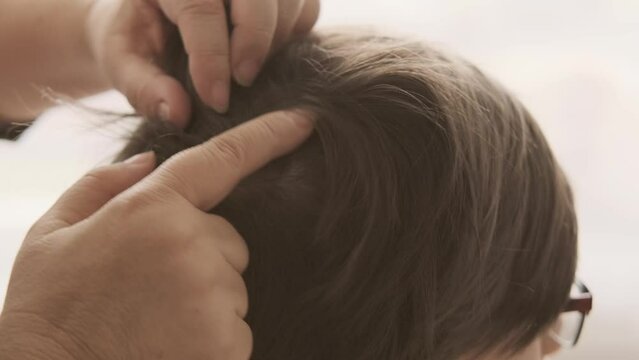 Parent's hands checking school-age child's hair for insects, searching for lice and nits, close-up head, importance of regular checks and preventive care
