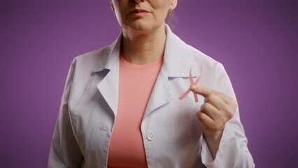 Woman doctor showing pink ribbon on purple background, breast cancer awareness