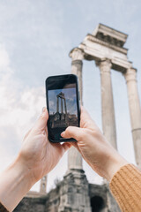 A person is taking a picture of a great columns of the roman forum with a smartphone