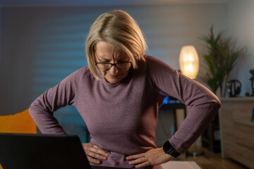Mature woman suffering from strong abdominal pain while sitting on sofa at home. Medical or...