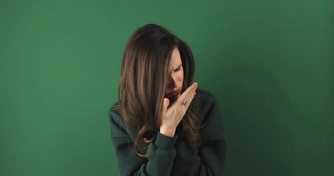 Woman wear green sweatshirt is suffering with cough and feeling bad on green background. Health care and safety. Millennial woman coughing hardly while hold neck.