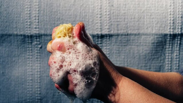 Hand squeezing natural sponge water soapy suds water