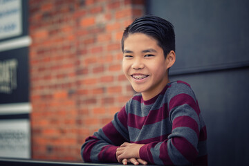 Happy, smiling teenage asian boy with braces leaning over outdoor railing.