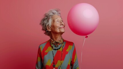 Obraz na płótnie Canvas An elderly woman with a satisfied expression on her face looks at the balloon. the woman is dressed in arena attire with short gray hair. Horizontal studio photo with pink background.