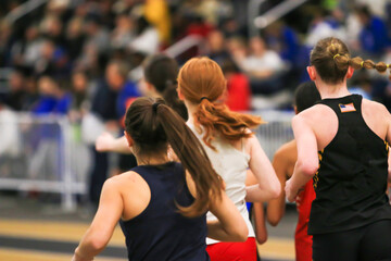 Rear view of girls running the mile on an indoor track