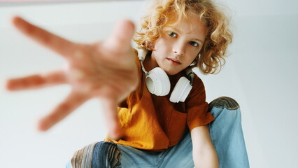Curly-Haired Child With Headphones Reaching Out to the Camera