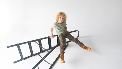 A young guy with curly hair poses sitting on a black metal staircase in a bright studio.