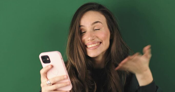 Attractive brunette woman look surprised wow hold using mobile cell phone on green background. Girl look on smartphone and doing winner gesture. Girl just found out big win news, point on phone, wow.