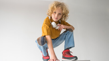 A boy with curly red hair is squatting with headphones around his neck