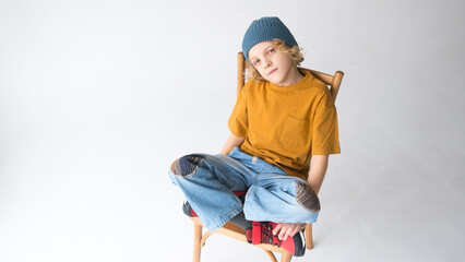Young boy in denim jeans and shirt, smiling with crossed legs on chair