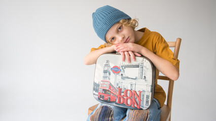 Young boy happily sits on chair with London suitcase in hand