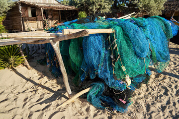 Fishing nets are getting dry on sun over simple wooden poles, small hut in background. Typical...