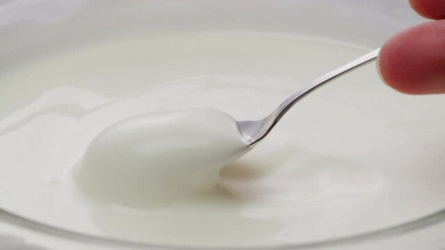 White creamy sauce texture close-up. Dip a spoon into white yogurt macro. Dairy products concept. 