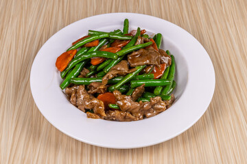 A plate of Chinese food, beef and green beans with vegetables on a wooden table