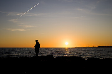 Ragazzo gurda il tramonto dagli scogli a Marina di Ragusa