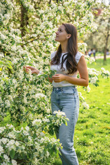 Young woman standing in the park near a pear tree that has blossomed with white flowers in the spring in Prague