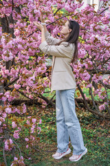 Young woman standing in the park near a sakura tree that has blossomed with pink flowers in the spring in Prague.