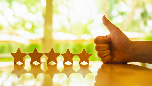 Five star symbols lined up on table with businessman giving thumbs up to show great rating and review.