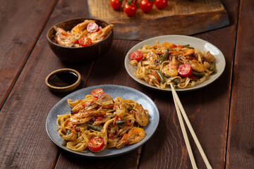 Rice with shrimp and udon in Pad Thai sauce on a wooden table next to cherry tomatoes, soy sauce and chopsticks