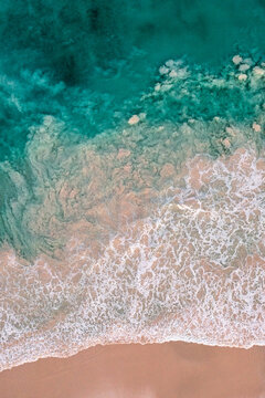Vertical top-down view of waves washing onto pink sand at Pink Sands Beach, Harbour Island, Bahamas