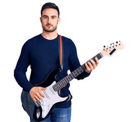 Young handsome man playing electric guitar thinking attitude and sober expression looking self confident
