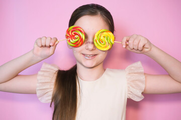 Portrait of happy smiling little girl with lollipop. Sugar for children. Little sweet tooth on pink background. Girl with bright makeup. Glittery glitter on face.