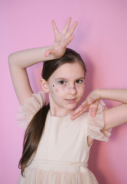 Cute happy girl with long hair with shiny freckles, rhinestones on her face, looking at camera, posing, fooling around, smiling cheerfully. Childish emotions with sparkling makeup. 