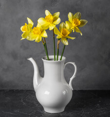 bouquet of yellow daffodil flowers in a light vase on a dark background