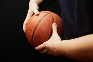 hands of a basketball player hold the ball to the side, shielding the ball in basketball, individual technique of shielding the ball in basketball on a black background, close-up, basketball training - obrazy, fototapety, plakaty