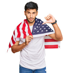 Young handsome man holding united states flag with angry face, negative sign showing dislike with...